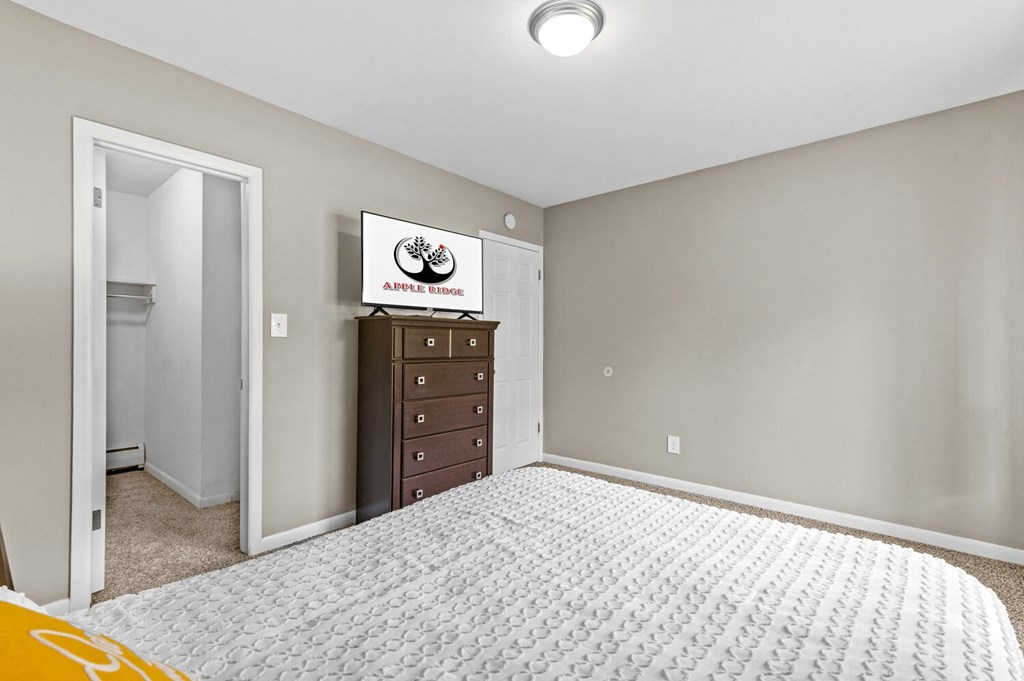 a bedroom with a large bed and a dresser at Apple Ridge Apartments - Livonia, MI, Livonia, MI, 48152