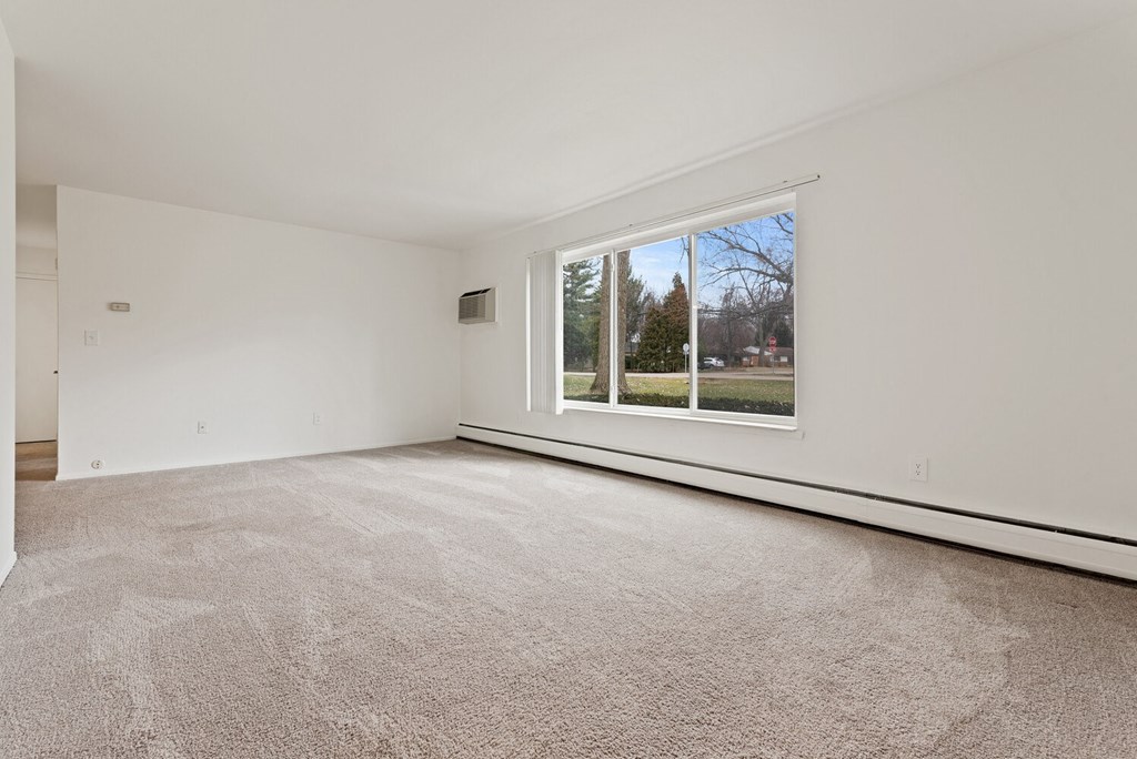 an empty living room with a large window and carpeting