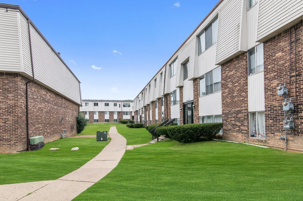 an exterior view of an apartment building with green grass and a sidewalk