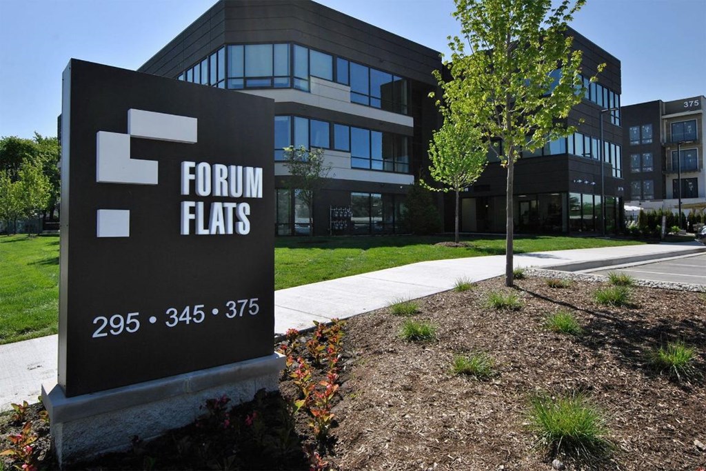 A sign for Forum Flats stands in front of a modern building.