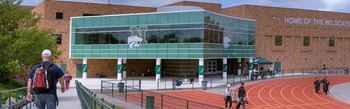 A group of people are walking on a track in front of a building that says Home of the Wildcats.