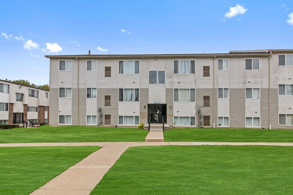 an apartment building with green grass and a sidewalk in front of it