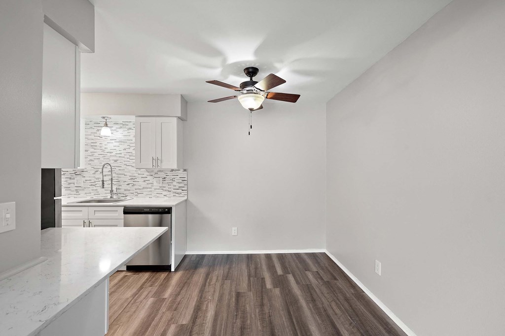 an empty living room with a ceiling fan and a kitchen