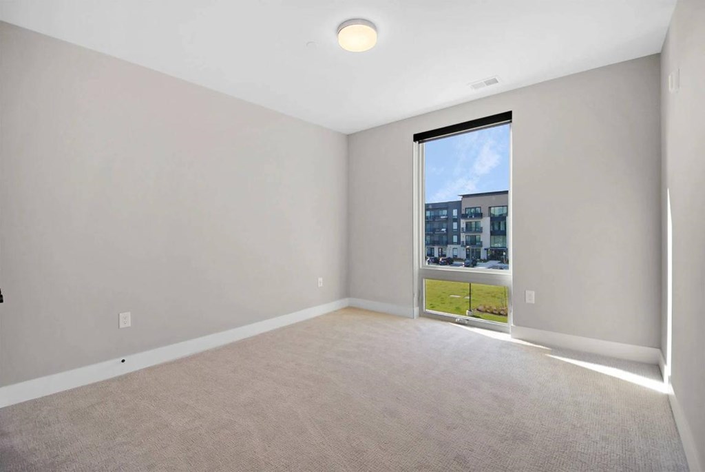 A room with a carpet floor and a window showing a view of a building.