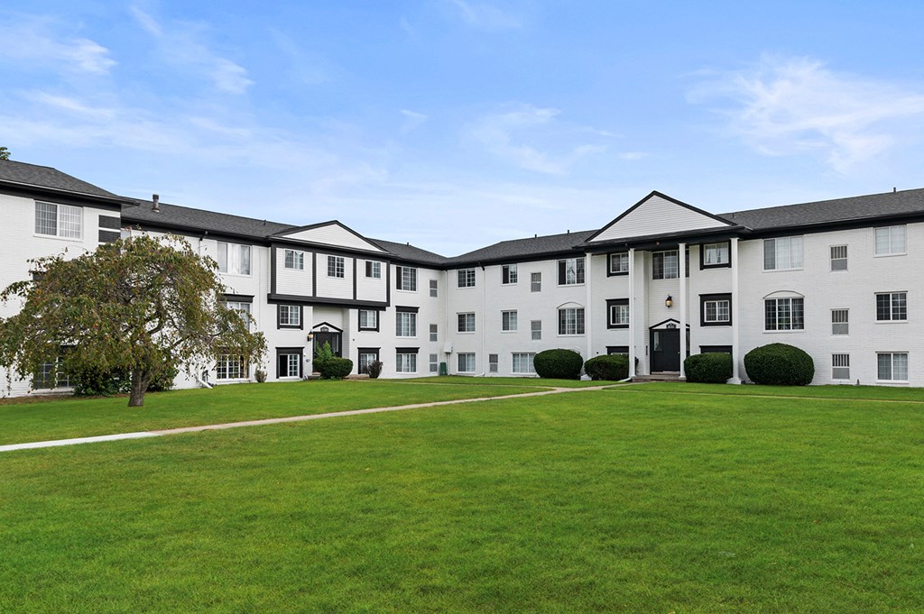 a large white building with a green lawn and a blue sky