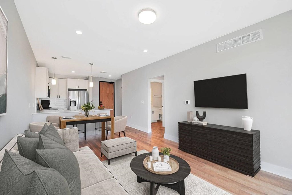 A modern living room with a grey sofa, a wooden coffee table, and a flat-screen TV mounted on the wall.