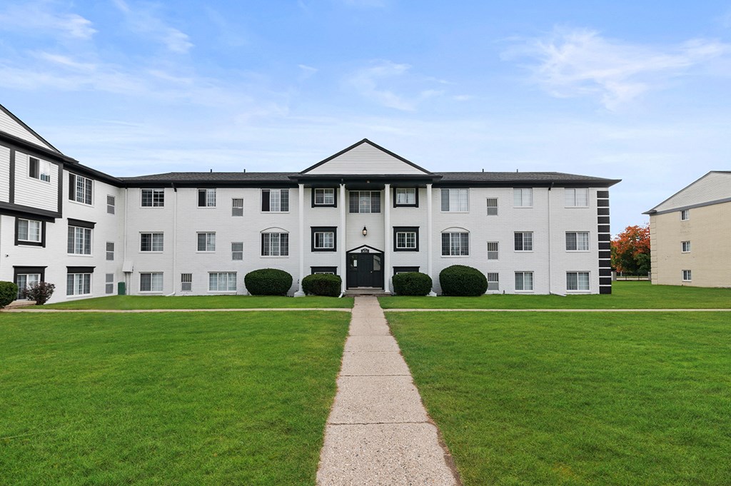 the front of a white building with a green lawn and a sidewalk