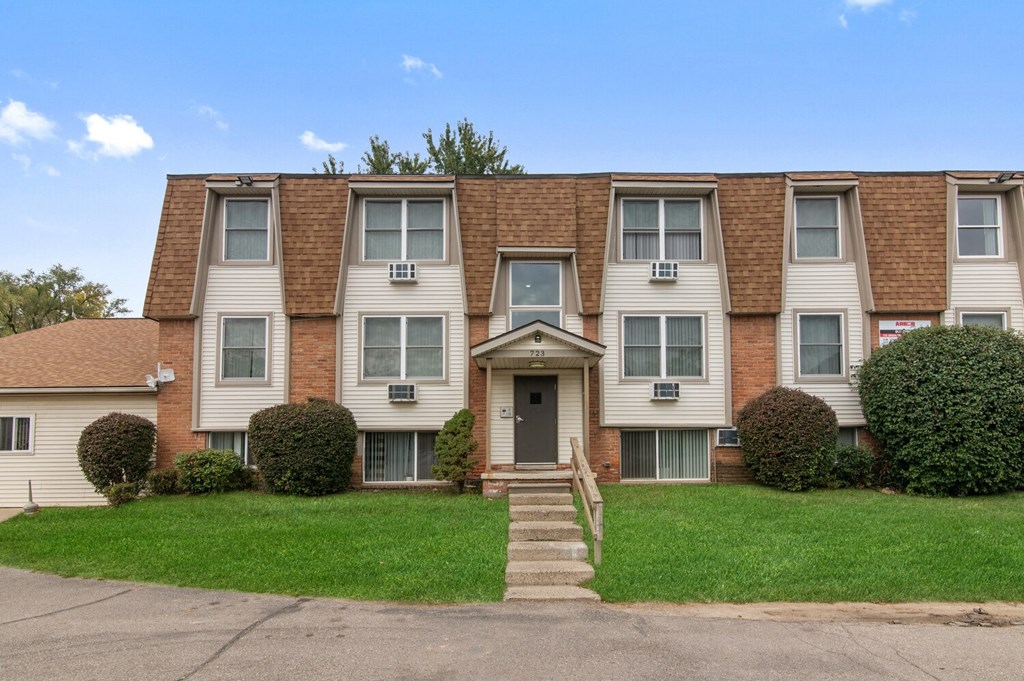 an apartment building with stairs in front of a green lawn