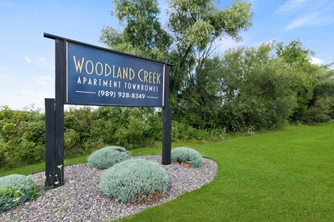 A sign for Woodland Creek Apartment Townhomes stands in front of a grassy area.