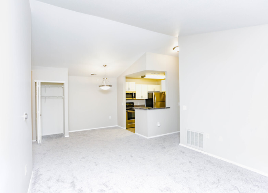 an empty living room with a kitchen in the background