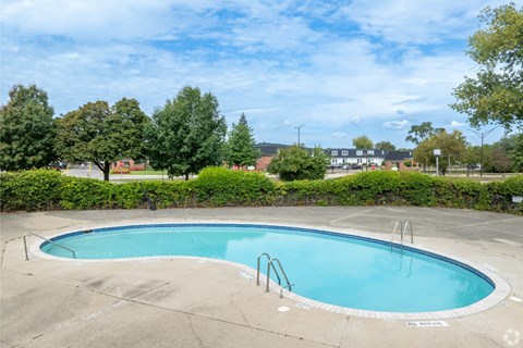 A small pool surrounded by a concrete deck and a hedge.