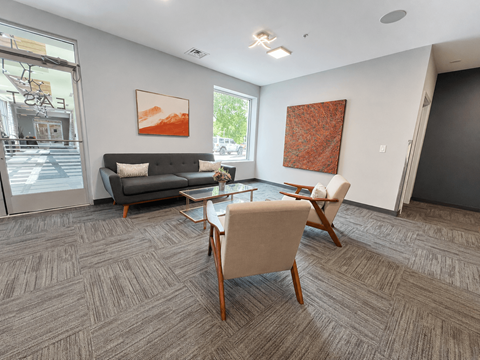 A living room with a grey sofa, a wooden table and chairs, and two pieces of artwork on the wall.