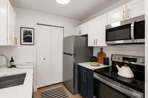 A modern kitchen with a stainless steel refrigerator and oven, white cabinets, and a black and white framed picture on the wall.