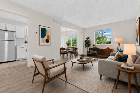 A modern living room with a white refrigerator, a wooden chair, a grey sofa, and a painting on the wall.