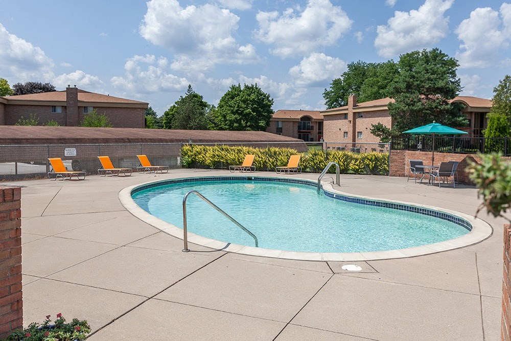 an oval swimming pool with orange chairs and a building in the background