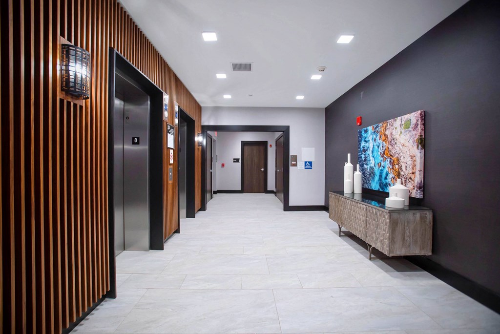 a hallway with elevators and a painting and a table with vases