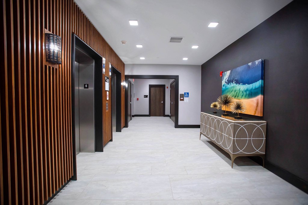 a hallway with elevators and a table with a painting in a lobby