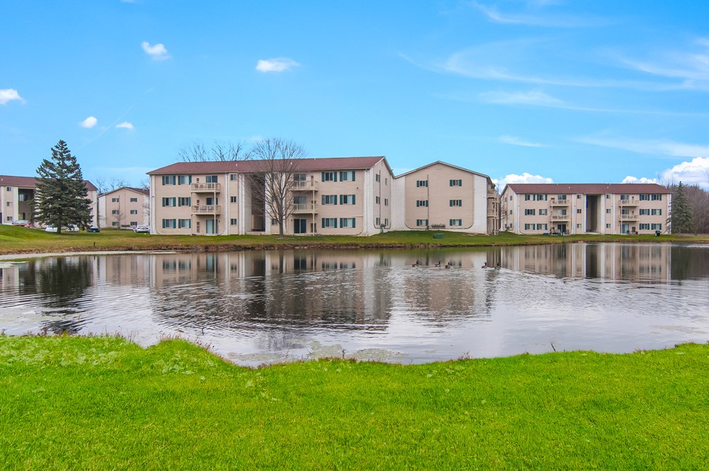 a large lake in front of some apartments with a blue sky