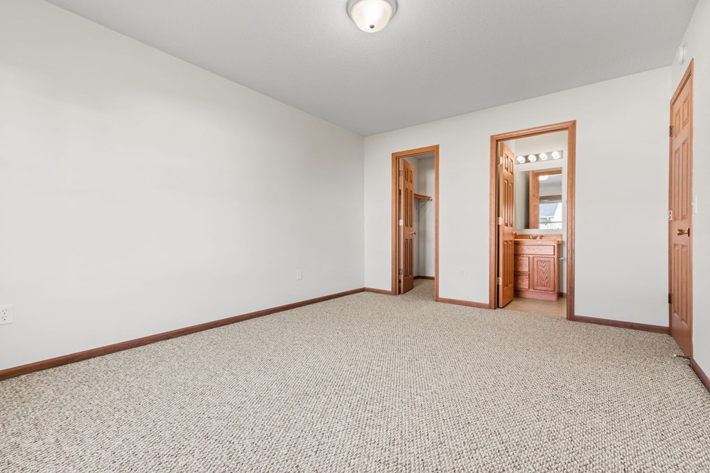 a living room with white walls and carpet and a door to a bathroom