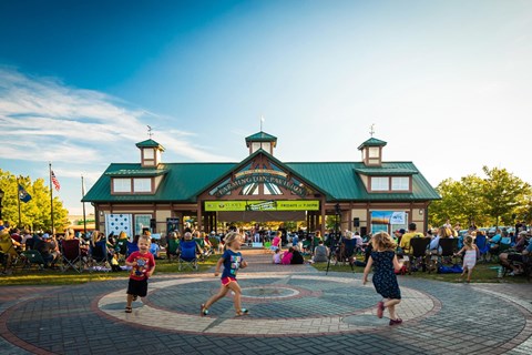 A group of people are dancing in a circle in front of a building with a green roof.