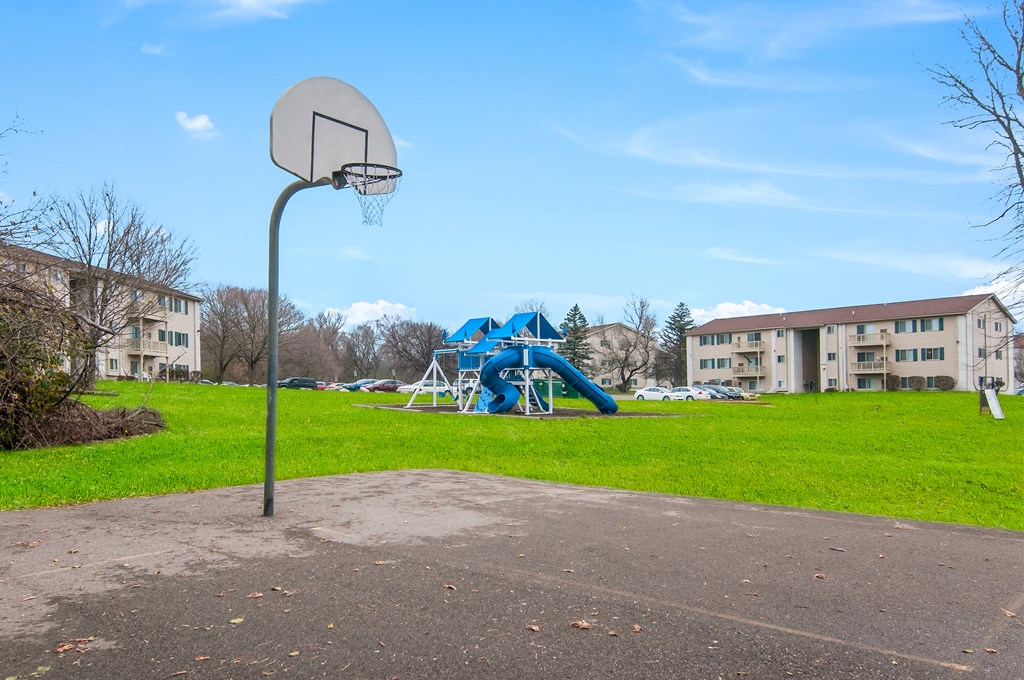 a basketball hoop in a park with a blue playground and apartment buildings