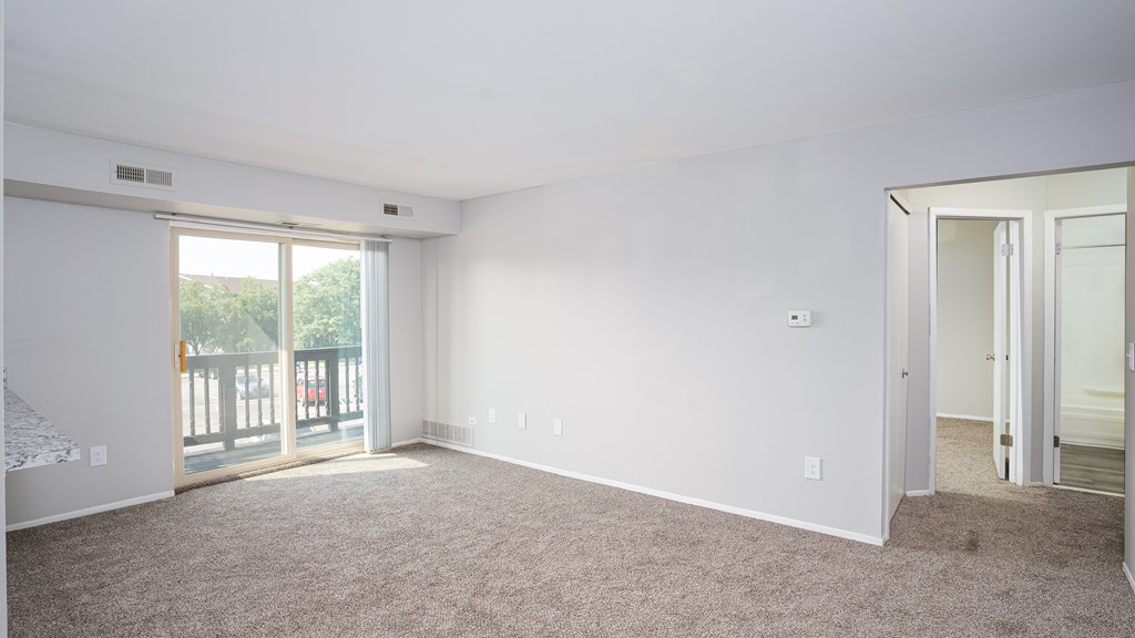 A large, empty room with a carpeted floor and a sliding glass door leading to a balcony.