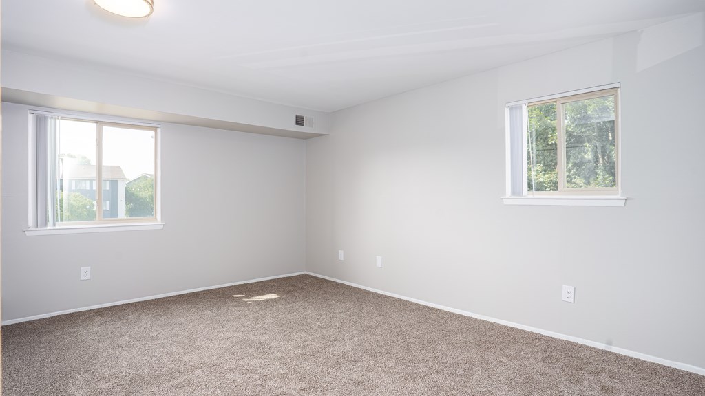 A room with carpeted floor and two windows.