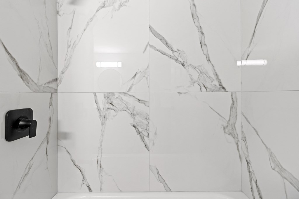 A white marble bathroom with a black faucet.