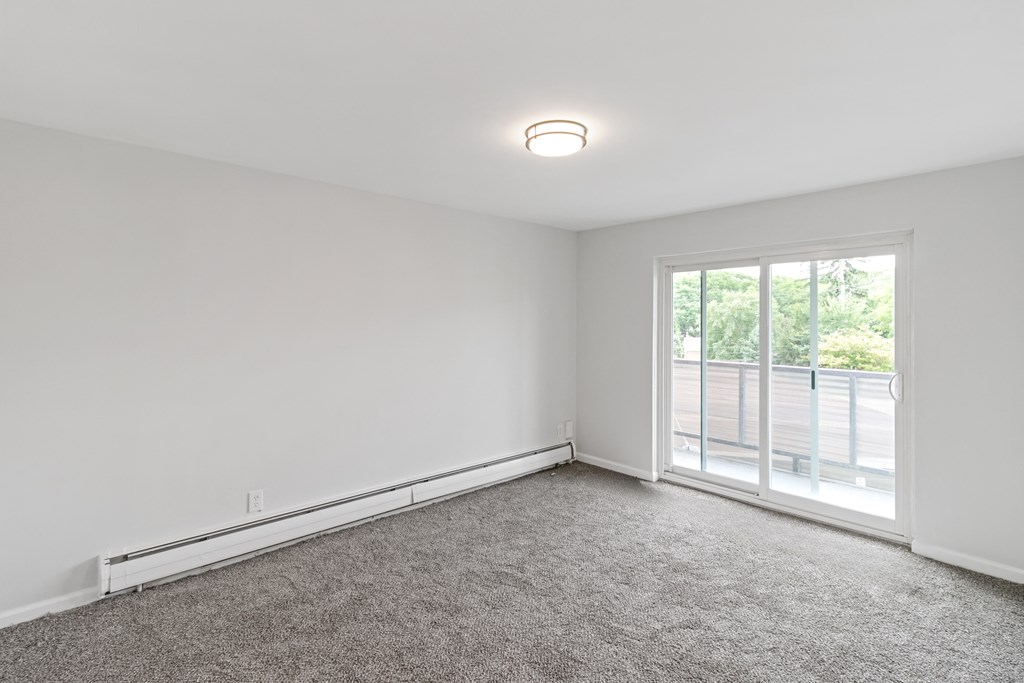 A room with a carpeted floor and a window overlooking a parking lot.