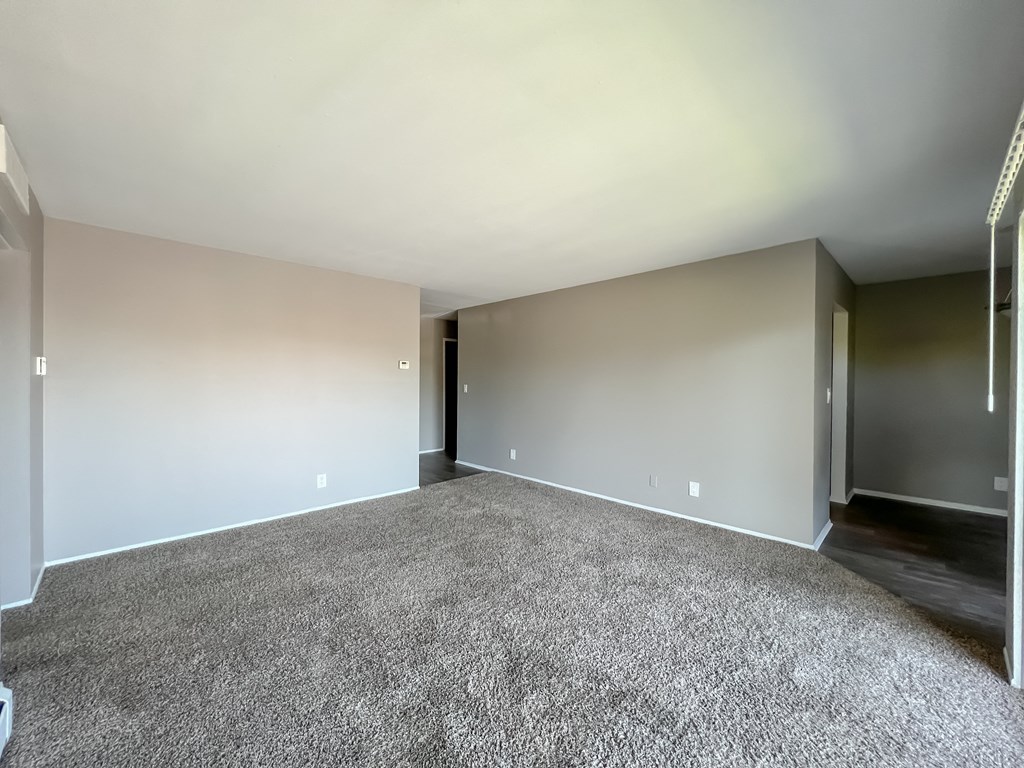 an empty living room with a carpeted floor and a hallway in the background