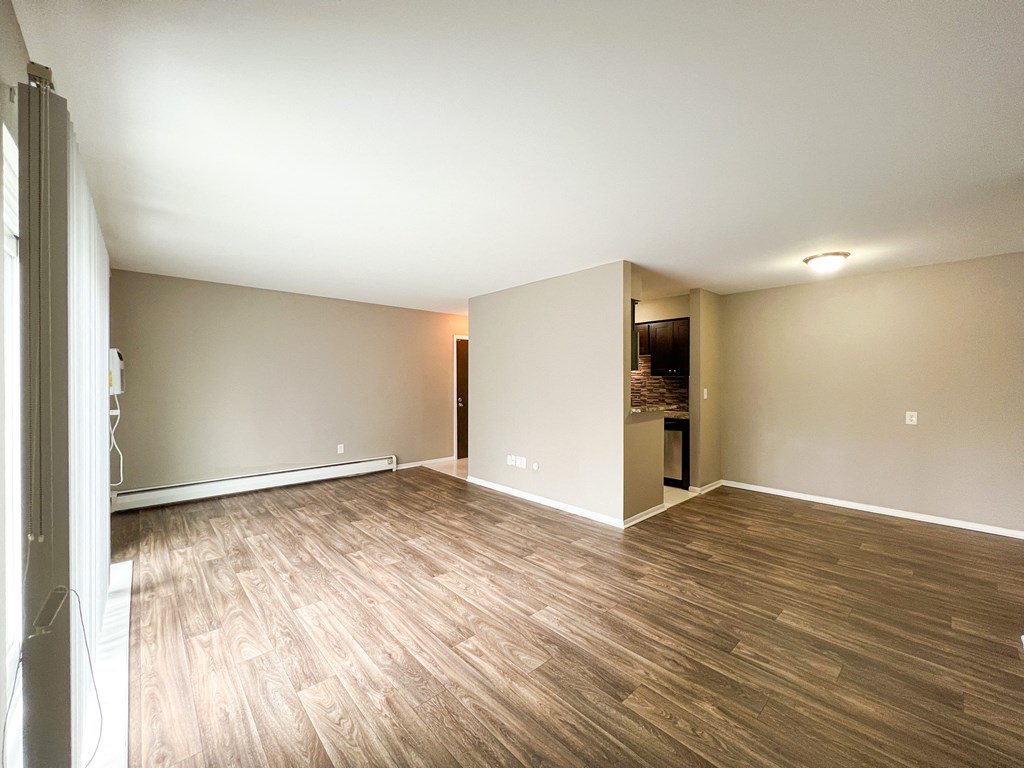 an empty living room with hardwood floors and a kitchen in the background