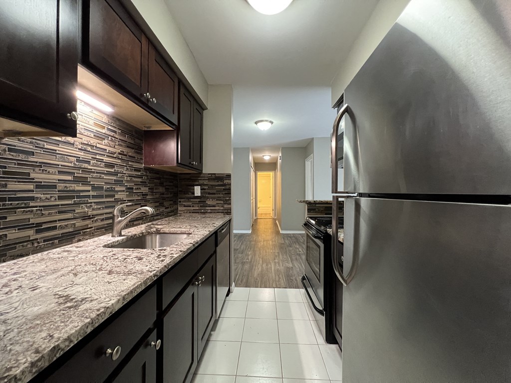 a kitchen with dark cabinets and a white tile floor at Apple Ridge Apartments - Livonia, MI, Livonia, MI