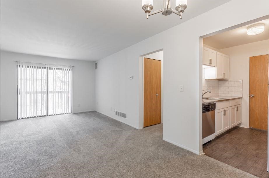 an empty living room with a kitchen in the background