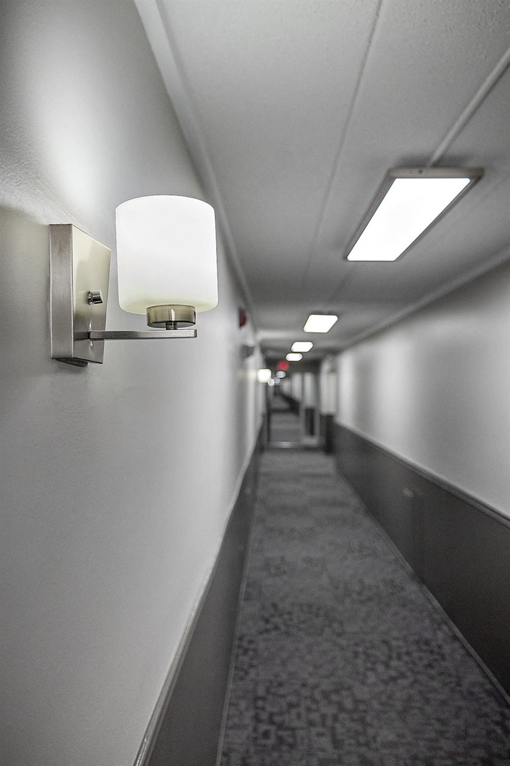 a long narrow hallway with lights on the wall and a carpeted floor at Troy Place Apartments - Troy, MI, Troy
