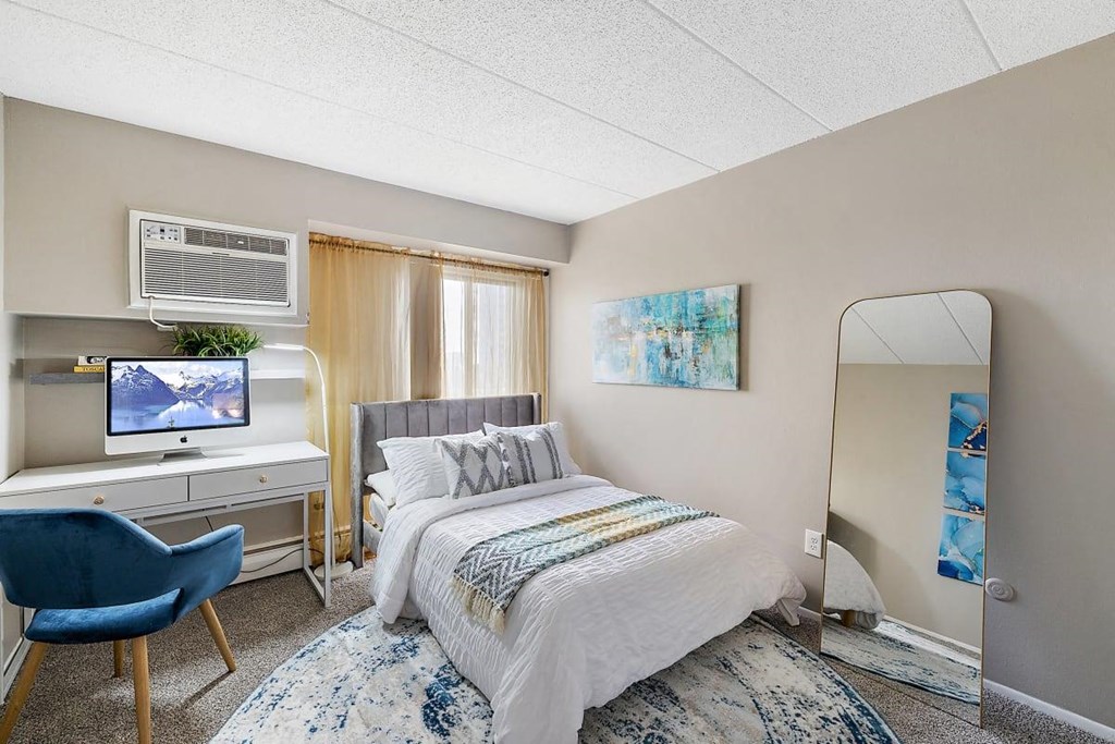 a bedroom with a bed and a desk with a mirror at Troy Place Apartments - Troy, MI, Troy, 48084