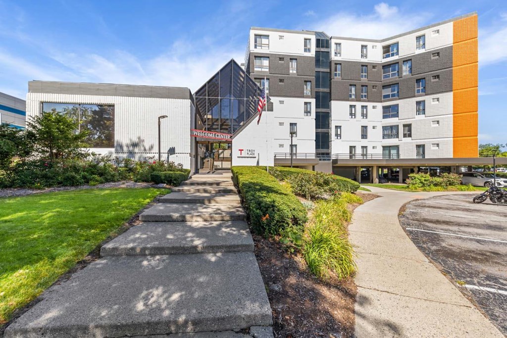 a sidewalk in front of a building with a flag at Troy Place Apartments - Troy, MI, Troy, Michigan