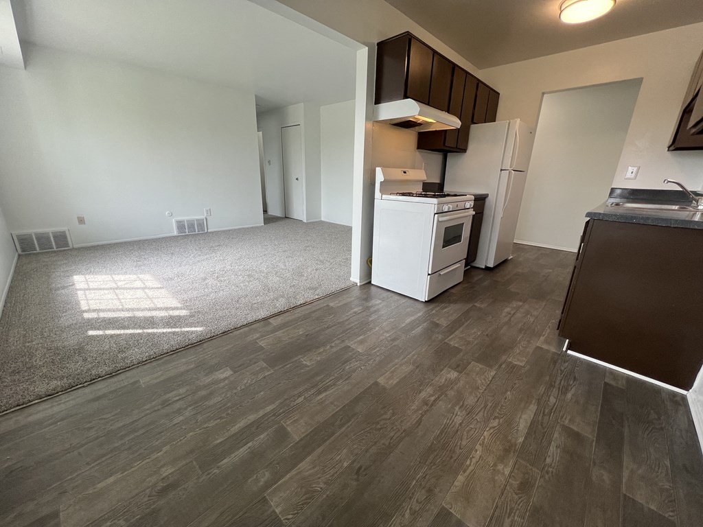 an empty living room with a kitchen in the background