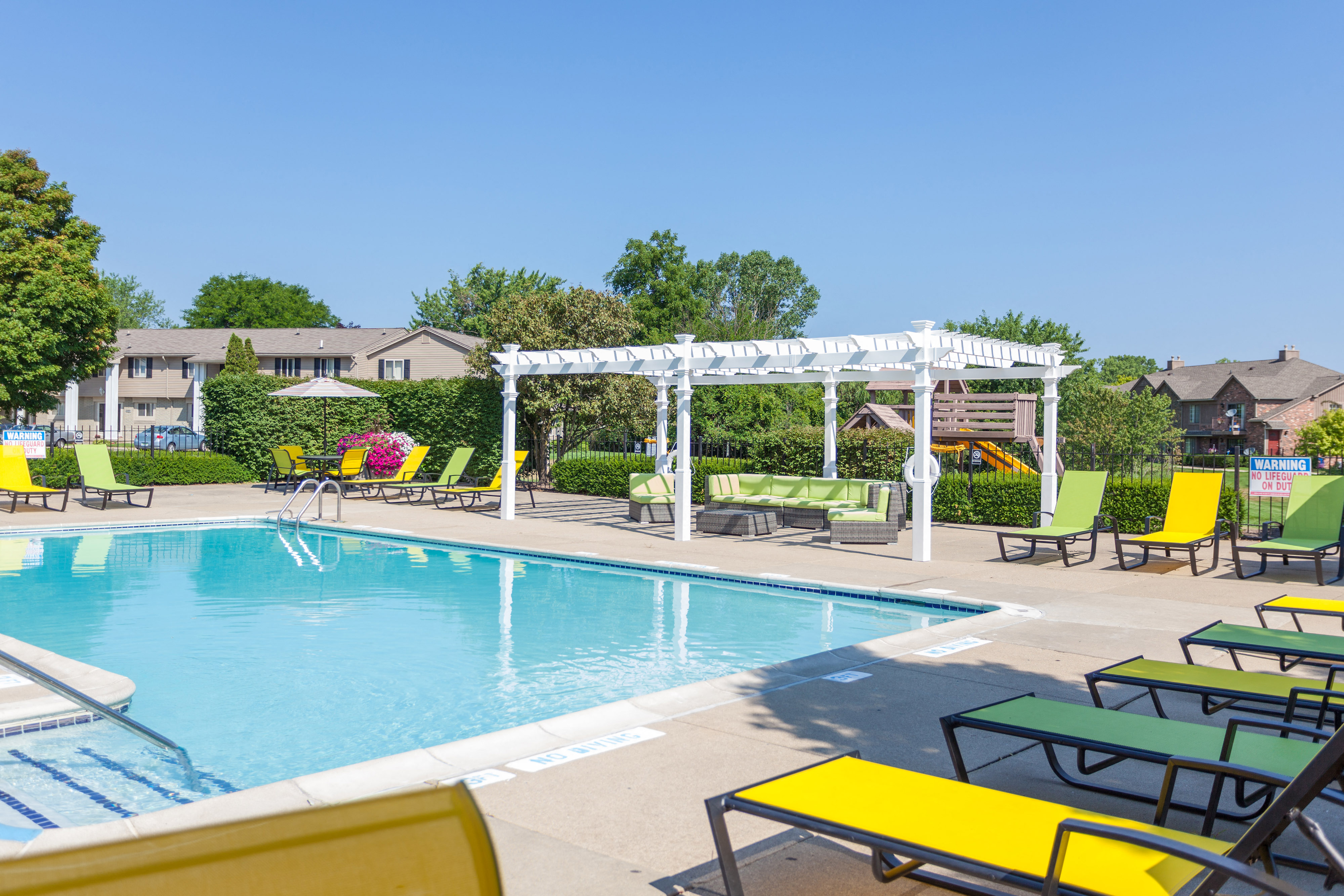 Swimming pool with pergola and colorful lounge chairs at Pilgrim Village - Canton, MI Apartments, Canton, Michigan