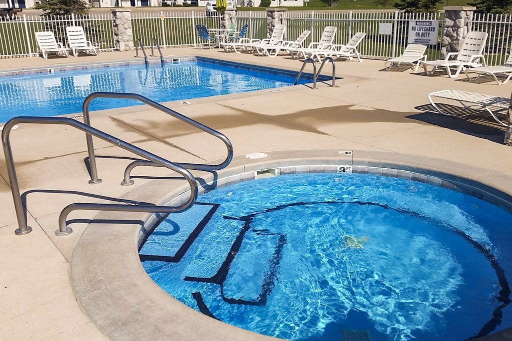 a pool with a hot tub and a swimming pool with chairs