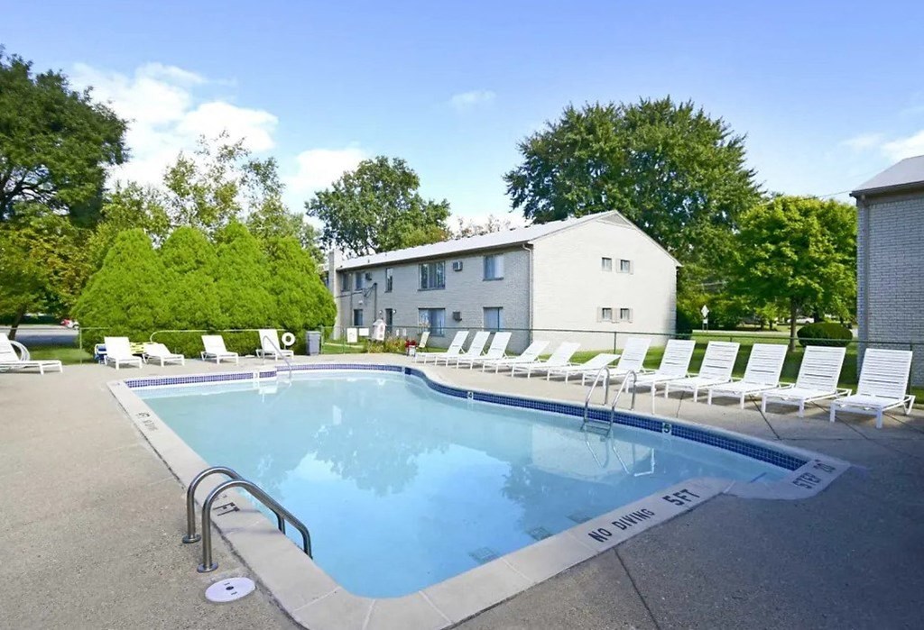a pool with white chairs around it in front of a building