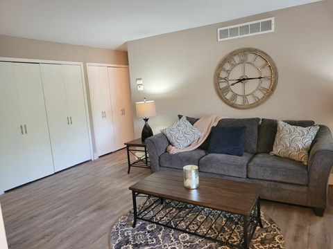 A living room with a grey couch, a coffee table, and a large clock on the wall.