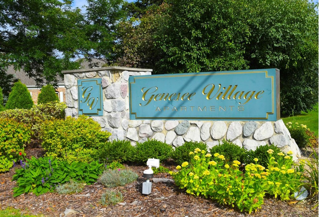 a sign for garden village apartments in front of a stone retaining wall