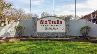 a sign for six trails apartments in front of a yard