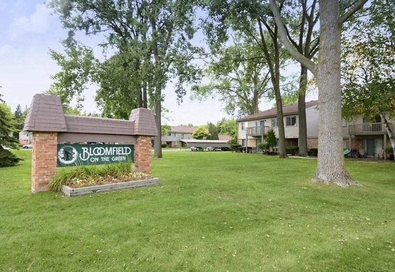 a sign for bloomer on the green in front of a yard with trees