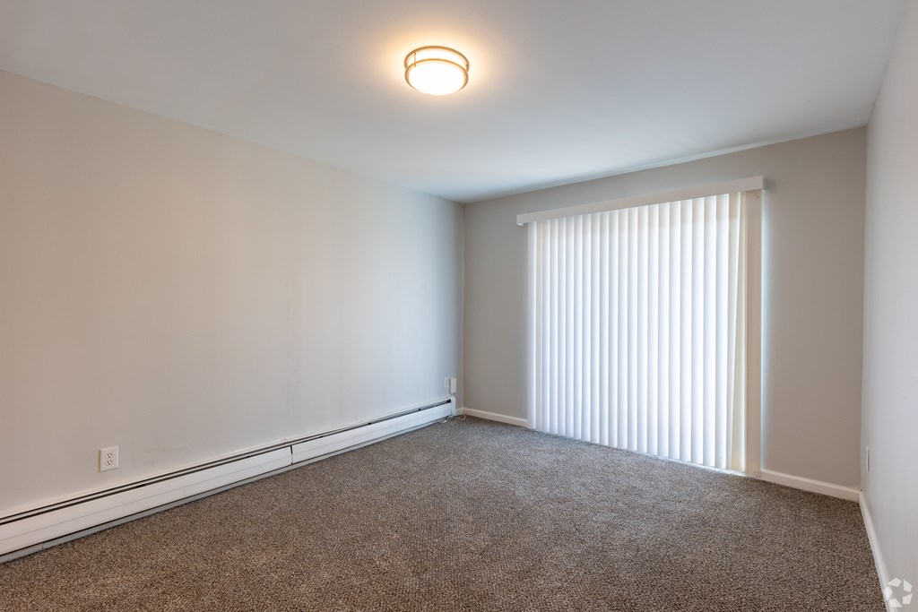 A room with a carpeted floor and a window with blinds.