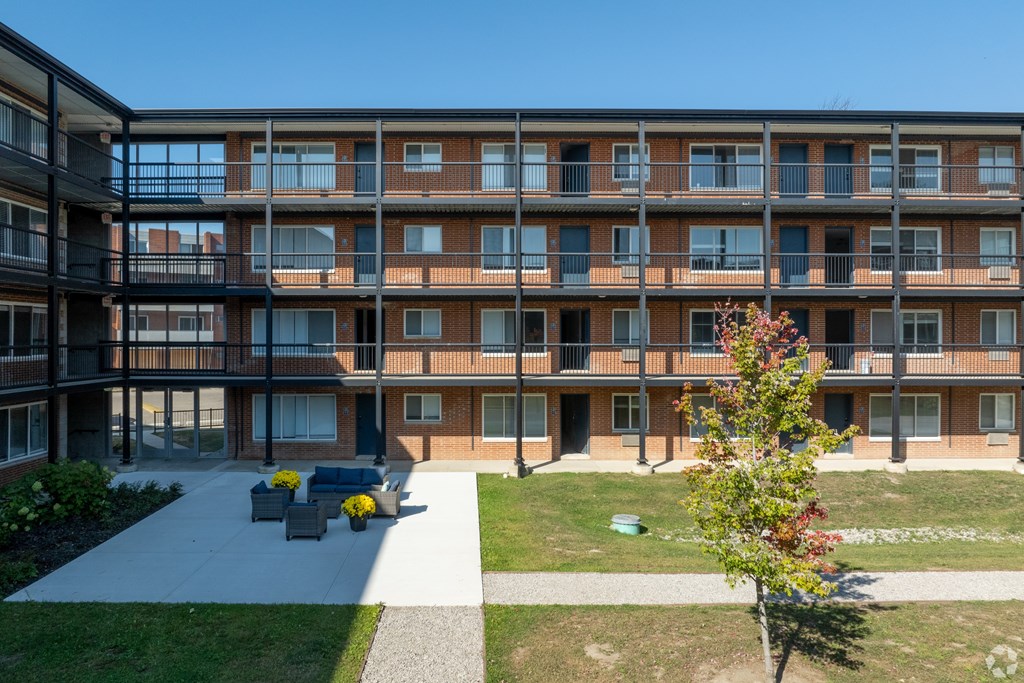 A tree with red leaves stands in front of a building with balconies.