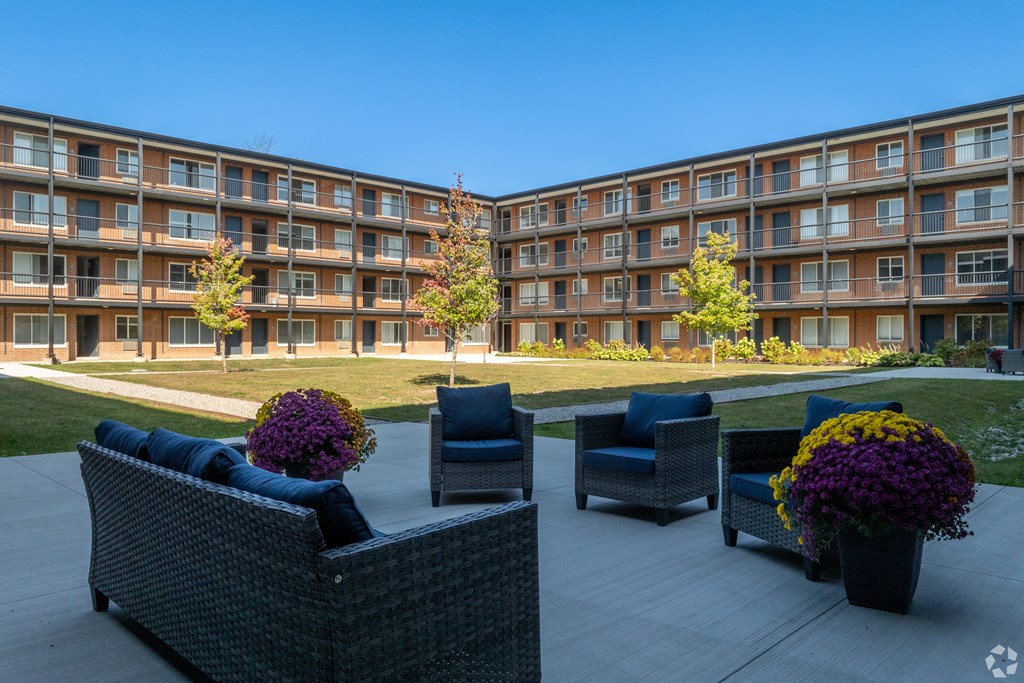A patio area with wicker furniture and potted plants in front of apartment buildings.