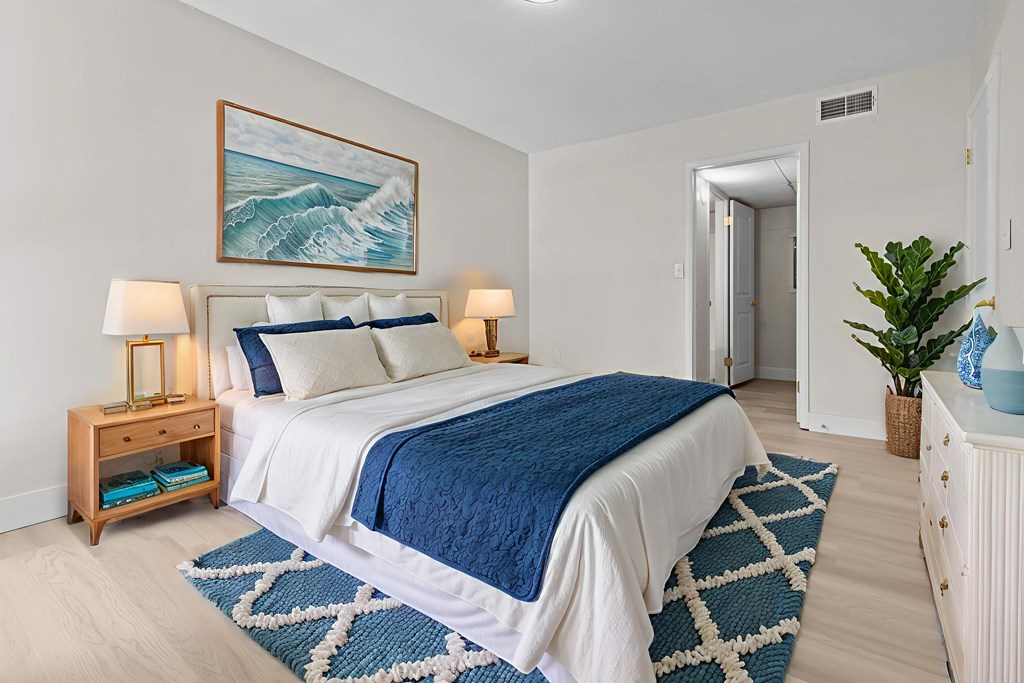 A bedroom with a large bed and a painting of a wave above it.