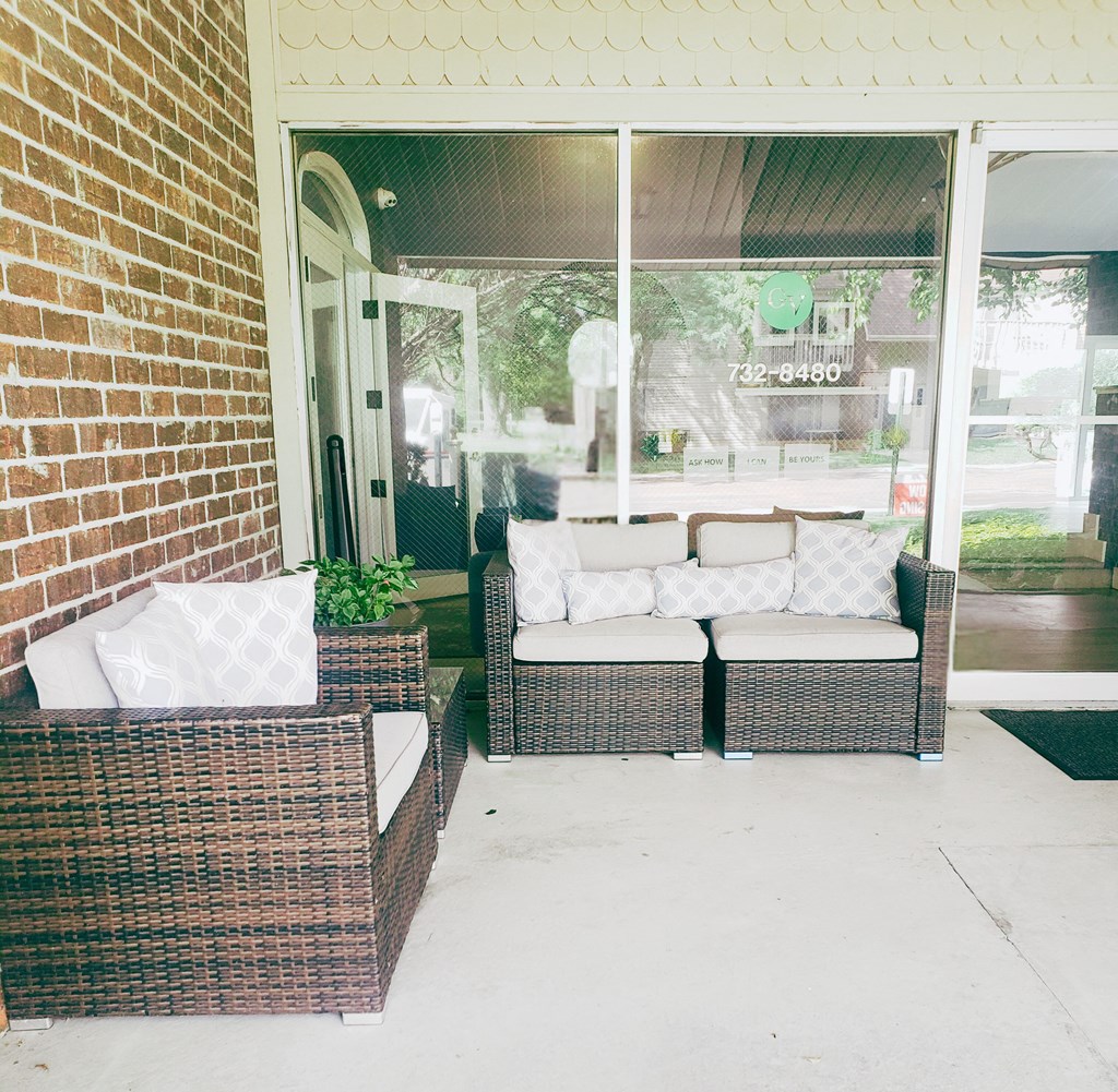 a porch with two rattan chairs and a brick wall