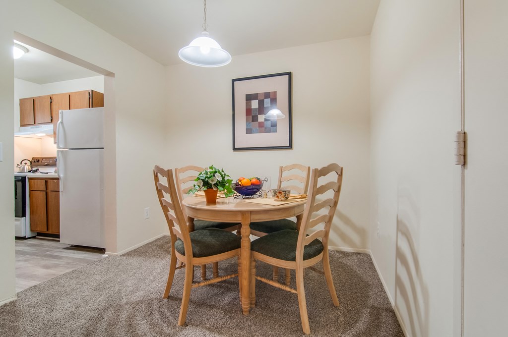 a dining area with a table and chairs and a kitchen with a refrigerator
